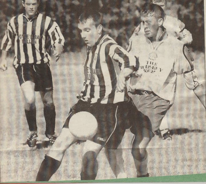Player shielding the ball from a striped opponent, newspaper photo