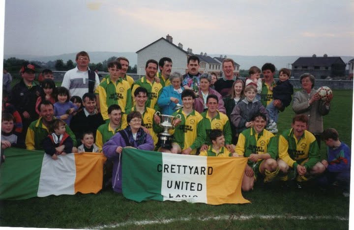 Crettyard United players, families and supporters celebrating with the cup behind a club flag
