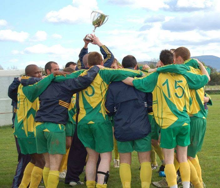 Crettyard United players huddled together on the pitch lifting the cup aloft